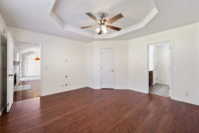 spare room with baseboards, ceiling fan, a tray ceiling, and wood finished floors