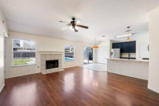 unfurnished living room with a tile fireplace, dark wood-style flooring, plenty of natural light, and ceiling fan