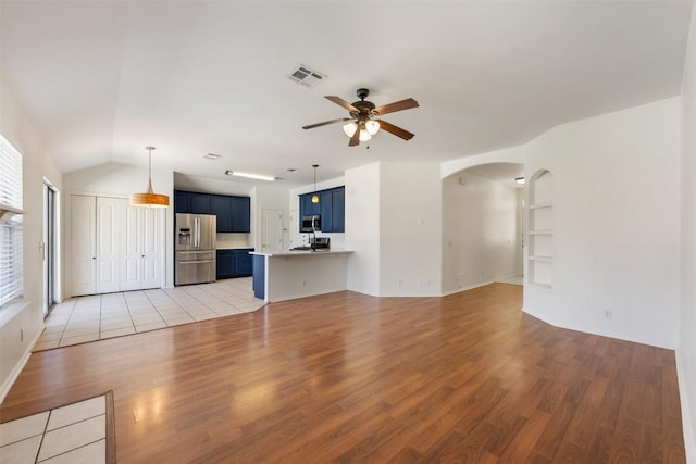 unfurnished living room featuring ceiling fan, lofted ceiling, built in shelves, visible vents, and light wood-type flooring