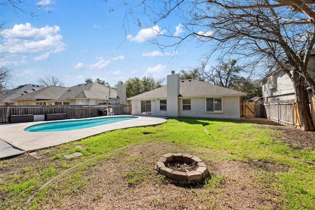 back of house with an outdoor fire pit, a fenced in pool, a fenced backyard, a chimney, and a yard