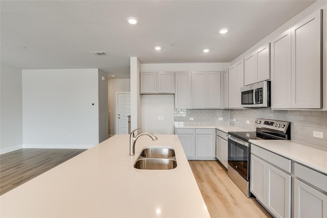 501 Emory Crossing Blvd, Hutto, TX 78634 - kitchen featuring appliances with stainless steel finishes, a sink, light wood-style flooring, tasteful backsplash, and light countertops