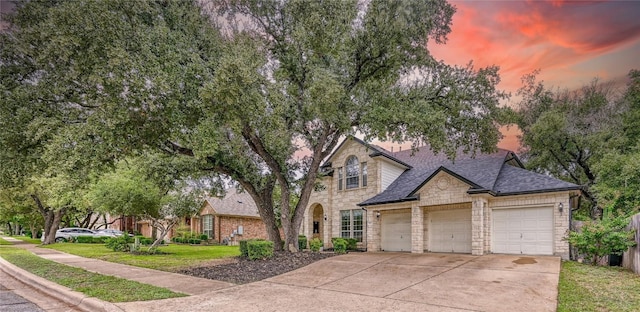 view of front of property featuring a garage, driveway, stone siding, roof with shingles, and a front yard