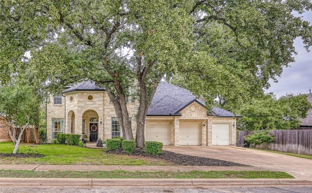 french provincial home with a garage, concrete driveway, stone siding, fence, and a front lawn