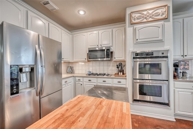 kitchen featuring appliances with stainless steel finishes, butcher block counters, visible vents, and decorative backsplash