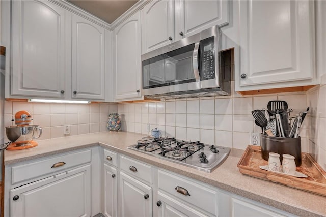 kitchen with stainless steel appliances, light countertops, white cabinets, and backsplash