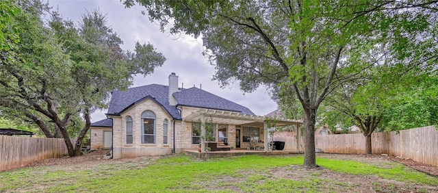 rear view of house featuring a lawn, a patio, stone siding, a fenced backyard, and a pergola