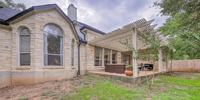 back of property featuring stone siding, a chimney, fence, a patio area, and a pergola