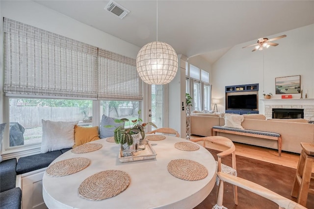 dining space featuring visible vents, wood finished floors, vaulted ceiling, a fireplace, and ceiling fan with notable chandelier