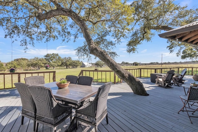 deck featuring outdoor dining area, a rural view, and a yard