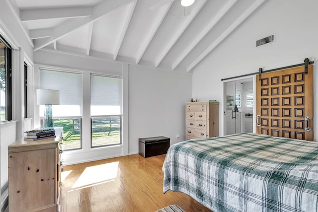 bedroom featuring light wood finished floors, visible vents, lofted ceiling with beams, and a barn door