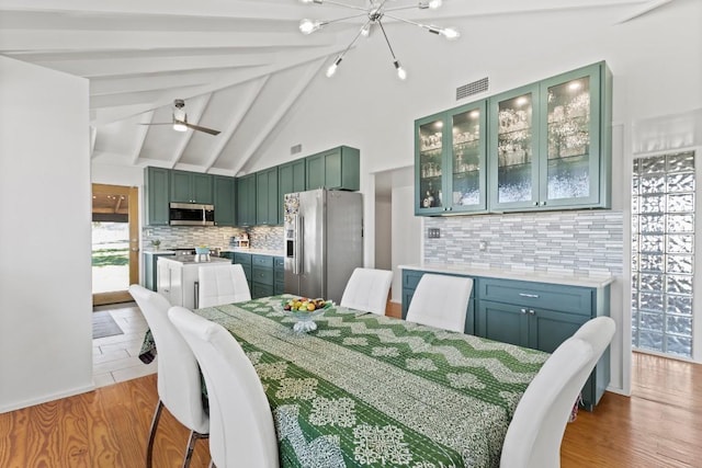 dining area with lofted ceiling with beams, visible vents, wood finished floors, and ceiling fan with notable chandelier