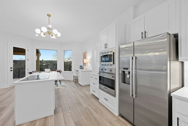 kitchen with light wood finished floors, white cabinets, appliances with stainless steel finishes, an inviting chandelier, and light countertops