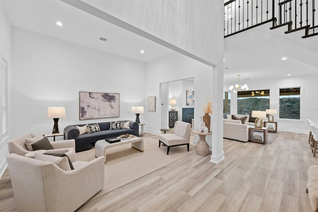 living area with recessed lighting, a notable chandelier, a towering ceiling, stairs, and light wood finished floors