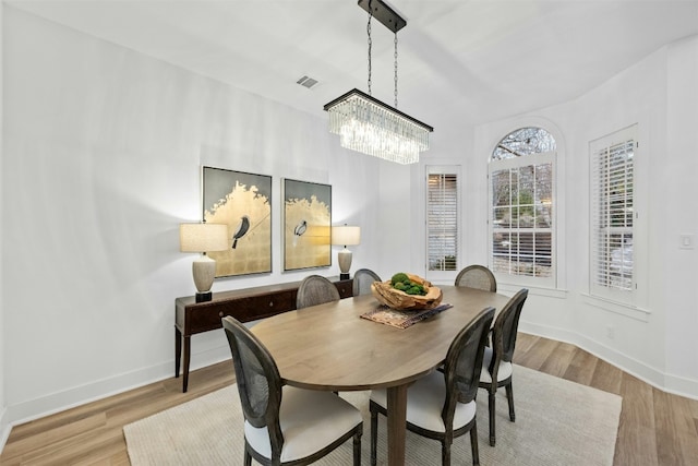 dining space with an inviting chandelier, baseboards, wood finished floors, and visible vents