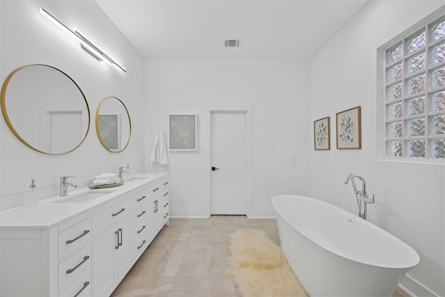 bathroom featuring double vanity, a soaking tub, visible vents, and a sink