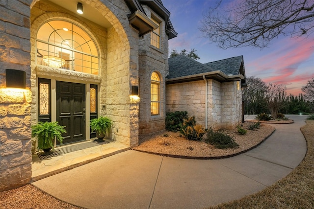 view of exterior entry with stone siding and roof with shingles