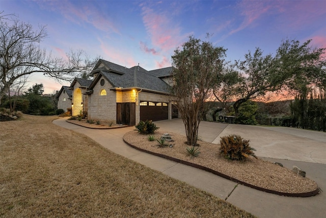 french country home featuring a garage, a shingled roof, a lawn, concrete driveway, and stone siding