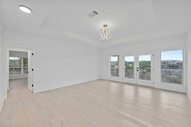 empty room featuring visible vents, a raised ceiling, a chandelier, and a healthy amount of sunlight