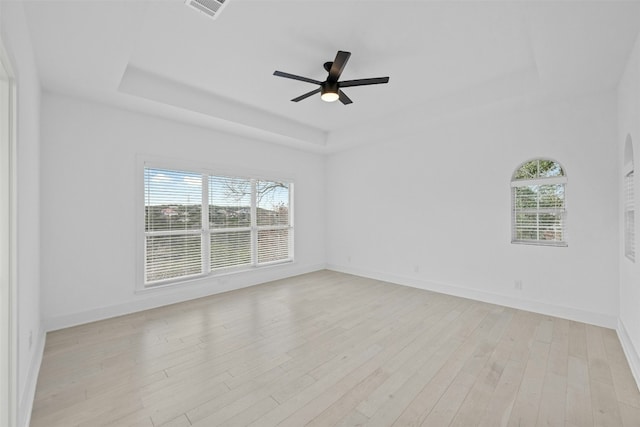 unfurnished room featuring plenty of natural light, visible vents, a tray ceiling, and light wood-style flooring