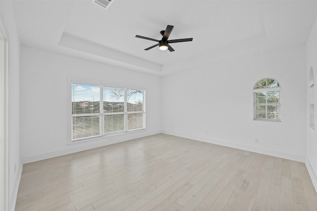 unfurnished room with visible vents, baseboards, a tray ceiling, a ceiling fan, and light wood-style flooring