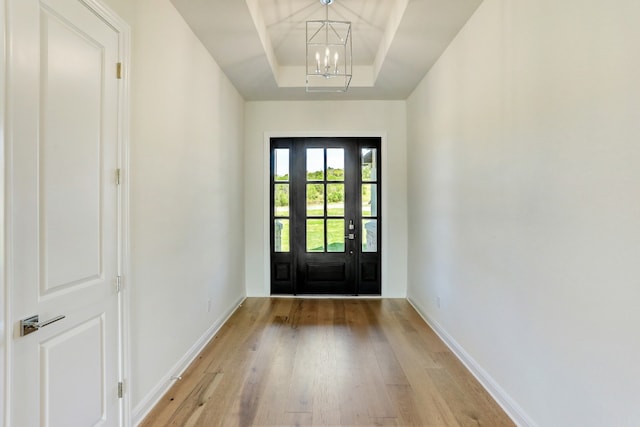 doorway to outside featuring an inviting chandelier, a raised ceiling, light wood-style flooring, and baseboards