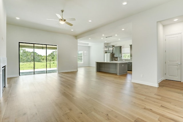 unfurnished living room with recessed lighting, a ceiling fan, baseboards, light wood-type flooring, and a glass covered fireplace