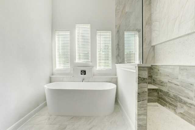 bathroom with marble finish floor, a soaking tub, baseboards, and walk in shower