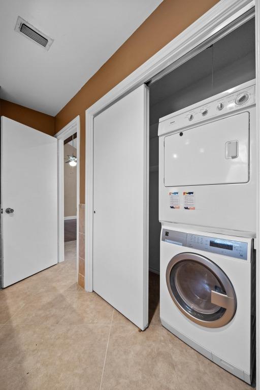 washroom featuring light tile patterned floors, stacked washer and clothes dryer, visible vents, and laundry area