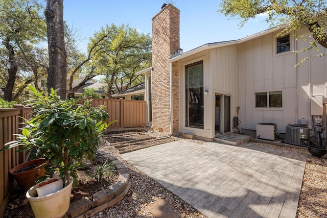 rear view of property with central AC unit, a chimney, fence, a patio area, and board and batten siding