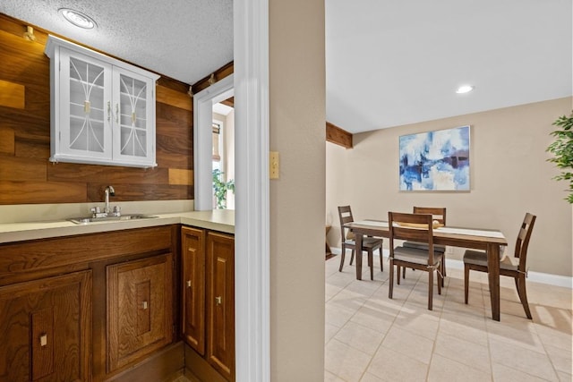 kitchen featuring light tile patterned floors, glass insert cabinets, light countertops, and a sink