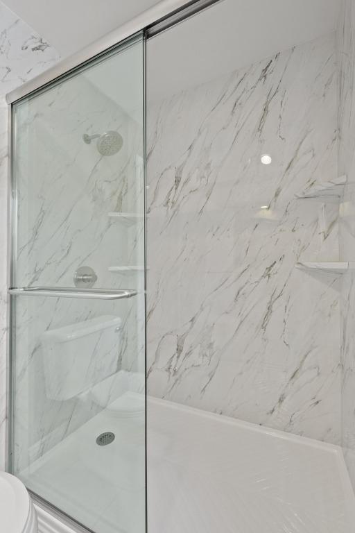 bathroom featuring a marble finish shower and toilet