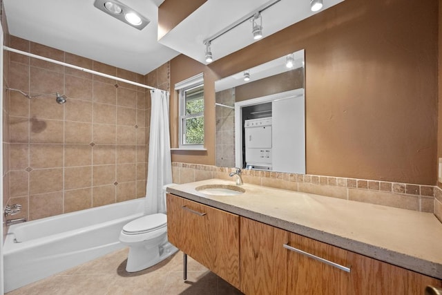 full bathroom with stacked washer and clothes dryer, shower / bath combination with curtain, toilet, vanity, and tile patterned flooring