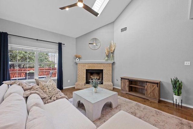 living area with visible vents, ceiling fan, wood finished floors, a brick fireplace, and high vaulted ceiling