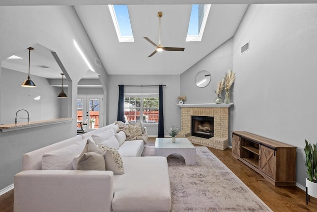 living area with a skylight, visible vents, dark wood-type flooring, a brick fireplace, and high vaulted ceiling