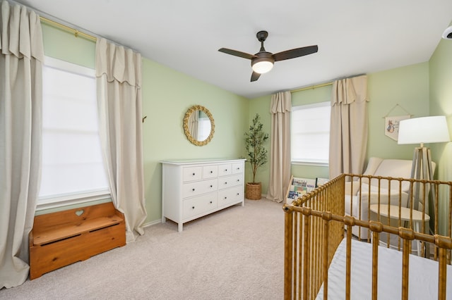 bedroom with a crib, a ceiling fan, and carpet flooring