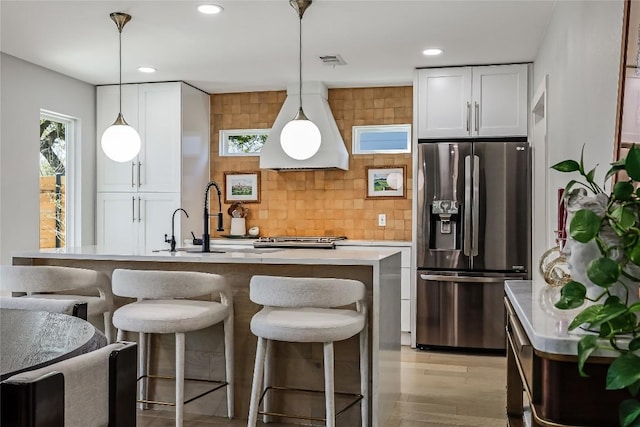 kitchen with premium range hood, visible vents, a kitchen breakfast bar, white cabinetry, and stainless steel fridge