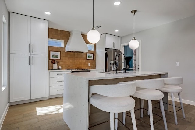 kitchen featuring light wood finished floors, backsplash, a sink, island range hood, and stainless steel fridge