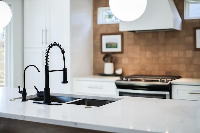 kitchen with tasteful backsplash, white cabinets, custom range hood, and stainless steel gas range oven