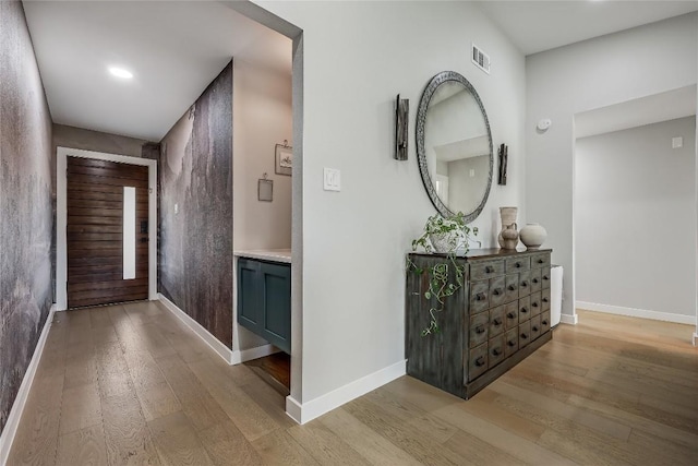 corridor with light wood-style floors, visible vents, and baseboards