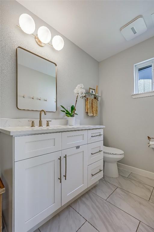 half bathroom featuring toilet, baseboards, and vanity