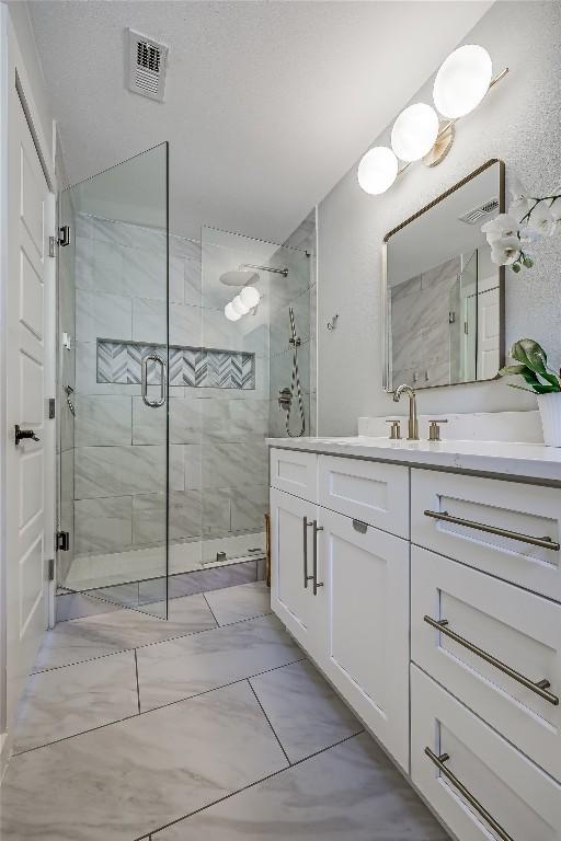 bathroom with marble finish floor, a shower stall, visible vents, and vanity