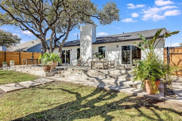 back of house featuring a lawn, a chimney, and fence