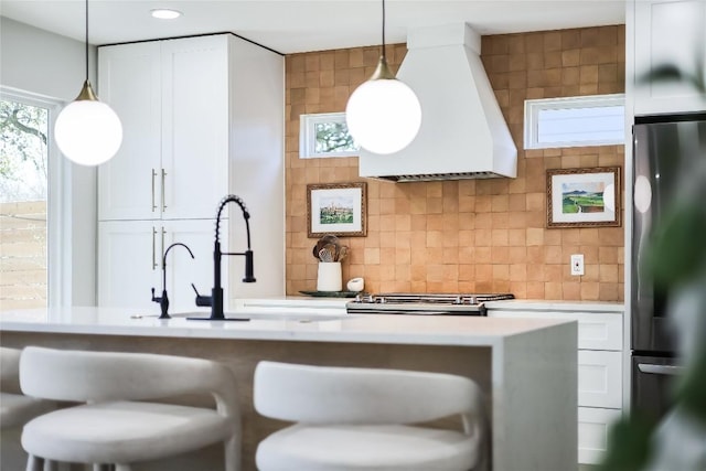 kitchen with white cabinets, freestanding refrigerator, custom exhaust hood, light countertops, and backsplash