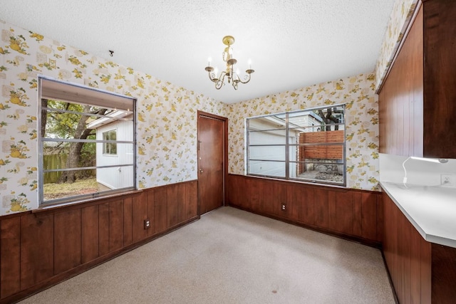 unfurnished dining area with a wainscoted wall, a textured ceiling, and wallpapered walls