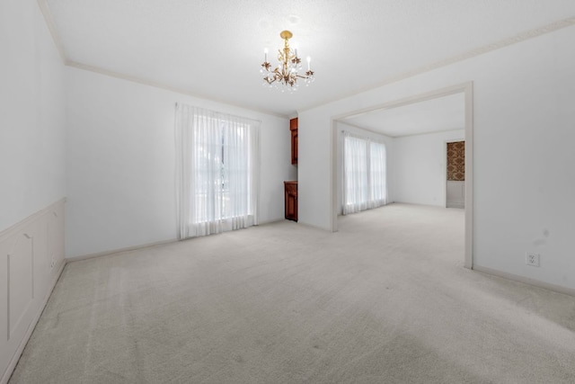 spare room featuring light carpet, an inviting chandelier, baseboards, and crown molding