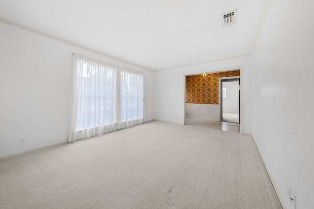 empty room featuring wallpapered walls, visible vents, baseboards, ornamental molding, and carpet