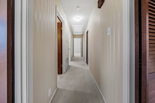 corridor featuring a textured ceiling, baseboards, and light colored carpet