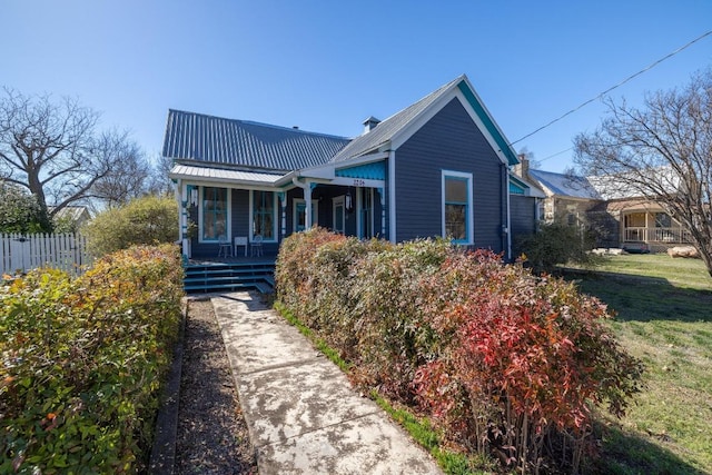 view of front facade with covered porch, a front lawn, fence, and metal roof