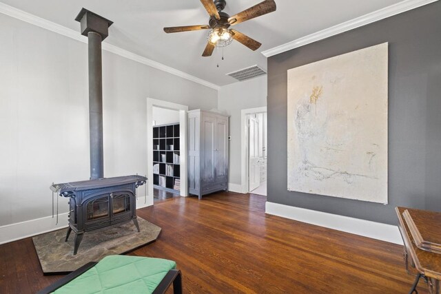 living area featuring a wood stove, visible vents, wood finished floors, and ornamental molding