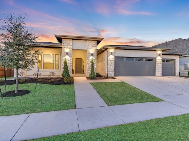 prairie-style home with a garage, stone siding, a lawn, and concrete driveway